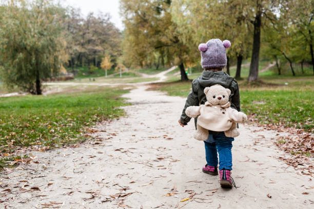 Little girl in autumn forest with teddy bear backpack. Fall day. Little girl exploring nature.