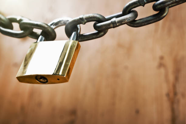 istock Brass padlock fastens metal chain against wood background 892670798