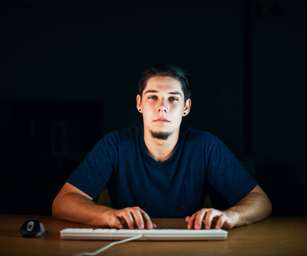 istock Young man working on computer at night stares at monitor 892671122