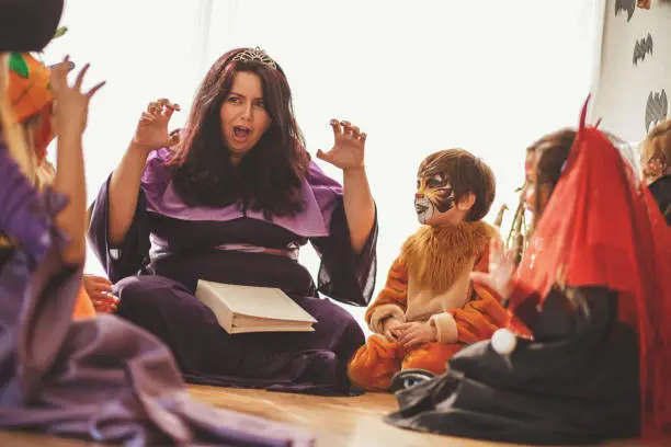 Woman is telling a story to group of children at the costume party.