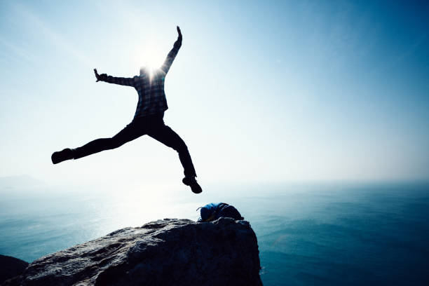 istock free female hiker jumping on sunrise seaside cliff edge 892673644