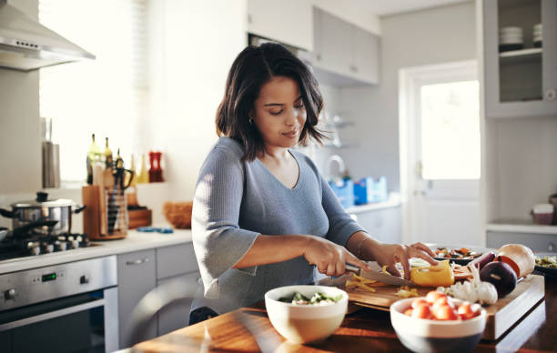 Preparing her favourite dish Shot of an attractive young woman cooking at home chopping food stock pictures, royalty-free photos & images