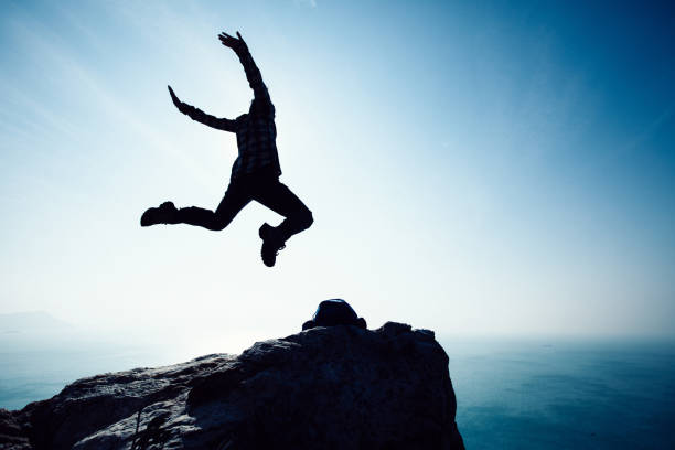 istock free female hiker jumping on sunrise seaside cliff edge 892674228