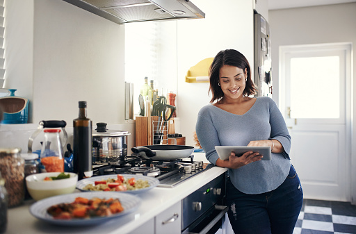 Shot of an attractive young woman using a digital tablet while cooking at home