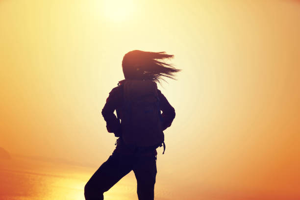 istock Young woman with backpack standing on sunrise windy coast 892698720