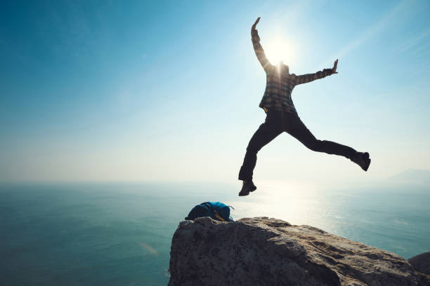 istock female hiker jumping on sunrise seaside cliff edge 892701008