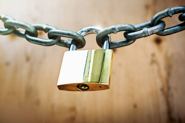 istock Brass padlock fastens metal chain against wood background 892706654