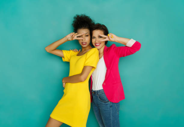 Two girlfriends fooling and dancing at turquoise studio background