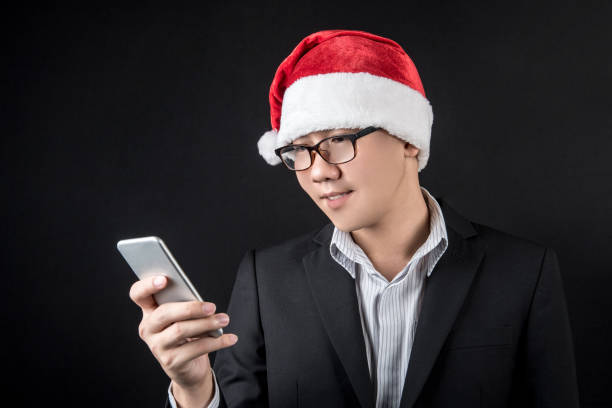 istock Young Asian businessman with santa hat using smartphone 892729150