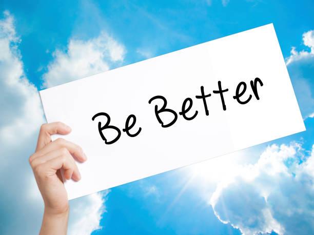istock Be Better Sign on white paper. Man Hand Holding Paper with text. Isolated on sky background 892746034