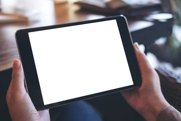 istock Mockup image of hands holding black tablet pc with white blank screen on wooden table background in cafe 892749546