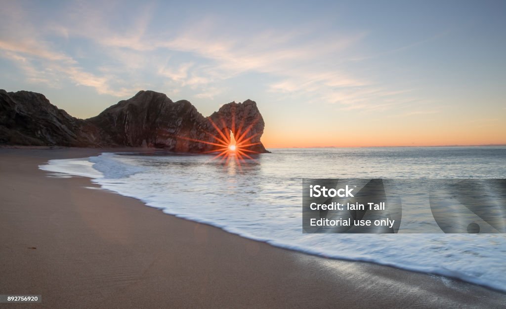 Durdle Door Sunrise on the Jurassic Coast The sunrise through the arch of Durdle Door in Dorset only happens during a brief period in the winter month of December, during the rest of the year the sun's alignment doesn't match the angle of the window of the arch, this and the weather plays havoc to plan this shot. Lulworth Cove Stock Photo