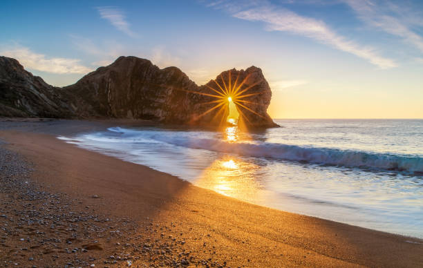 Durdle Door Sunrise on the Jurassic Coast The sunrise through the arch of Durdle Door in Dorset only happens during a brief period in the winter month of December, during the rest of the year the sun's alignment doesn't match the angle of the window of the arch, this and the weather plays havoc to plan this shot. durdle door stock pictures, royalty-free photos & images