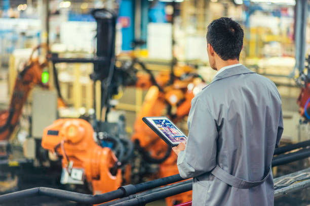 Engineer supervising autonomous producton process Rear view of an engineer in a gray coat looking at autonomous robotic arms while holding a digital tablet. hydraulic platform photos stock pictures, royalty-free photos & images