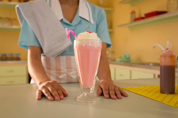 Capturing candid photograph in retro-themed diner setting with friends. One person holding vintage camera, another person enjoying milkshake and burger