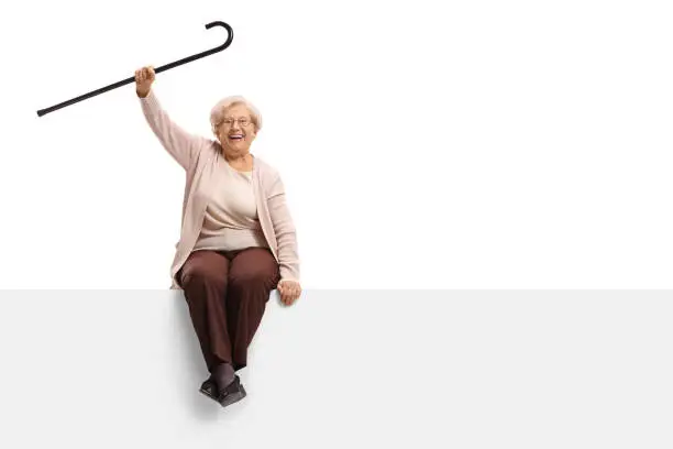 Photo of Overjoyed elderly woman with a cane sitting on a panel