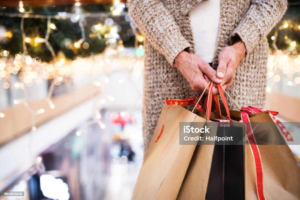 Senior woman with bags doing Christmas shopping. Unrecognizable senior woman with paper bags doing Christmas shopping. Shopping center at Christmas time. Shopping Stock Photo