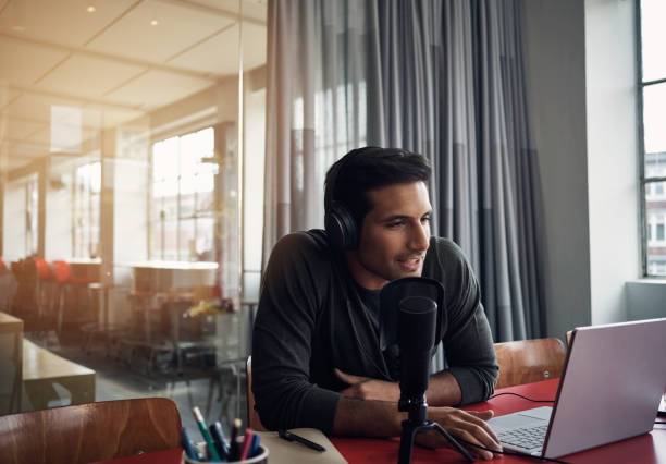 His company is joining the podcast craze Shot of a young man recording a podcast on a laptop in a modern office radio station photos stock pictures, royalty-free photos & images