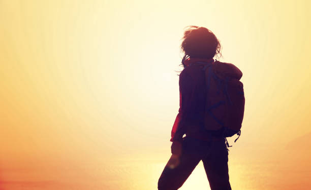 istock Young woman with backpack standing on sunrise windy coast 892813320
