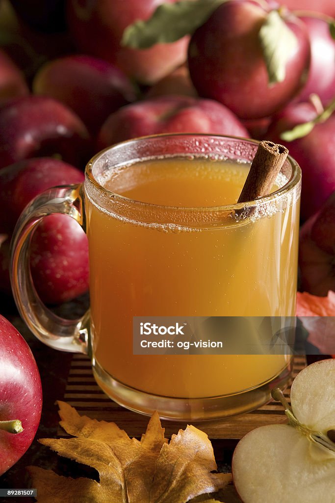 Apple cider in glass mug with cinnamon stick next to apples A cup of hot apple cider surrounded by red apples Hot Apple Cider Stock Photo