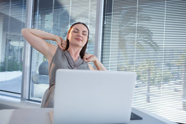 istock Tired female executive stretching her arms at desk 892816726