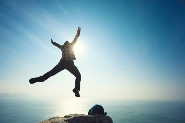 istock female hiker jumping on sunrise seaside cliff edge 892821616