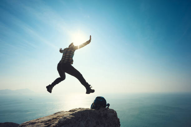 istock female hiker jumping on sunrise seaside cliff edge 892834928