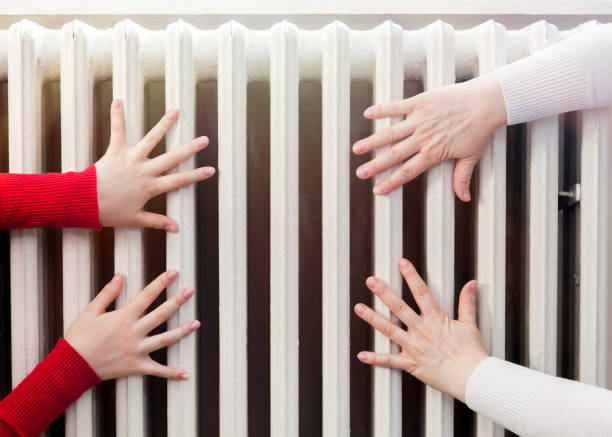 two pairs of female hands touching a radiator stock photo