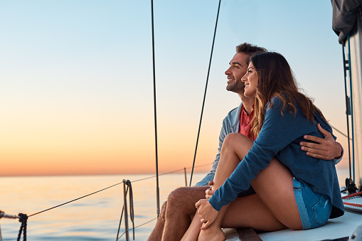 Young romantic couple sitting on the bow of a yacht during sunset. River travel and honeymoon concept