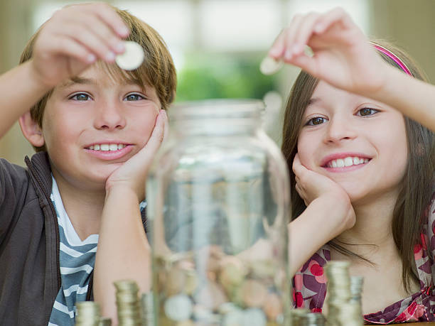 ragazzo e ragazza mettendo le monete in un barattolo di vetro - protection finance family wealth foto e immagini stock