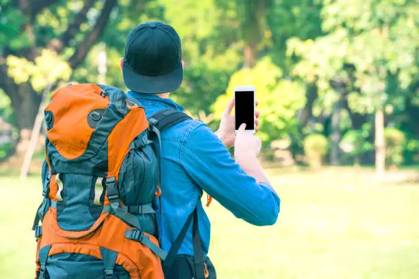 Tourist man with a backpack holding a phone in the nature. Digital nomad and travel tourism hike technology concept