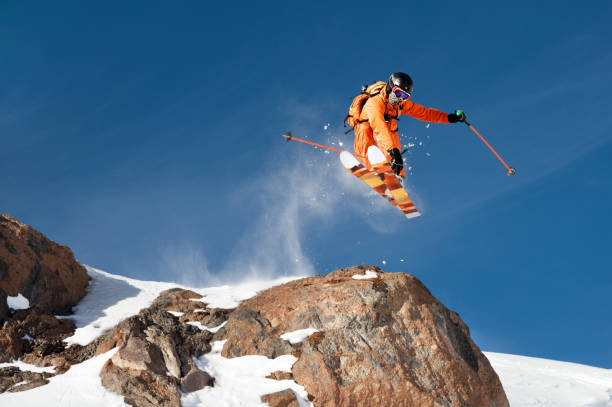 istock A professional skier makes a jump-drop from a high cliff against a blue sky leaving a trail of snow powder in the mountains 892921586