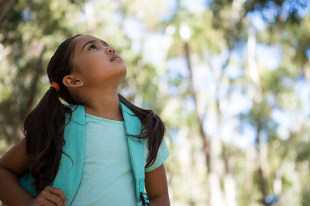 istock Little girl standing with backpack looking up in the sky 892944220