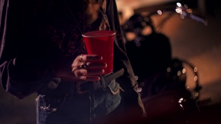 Young biker woman holding plastic cup at night music festival