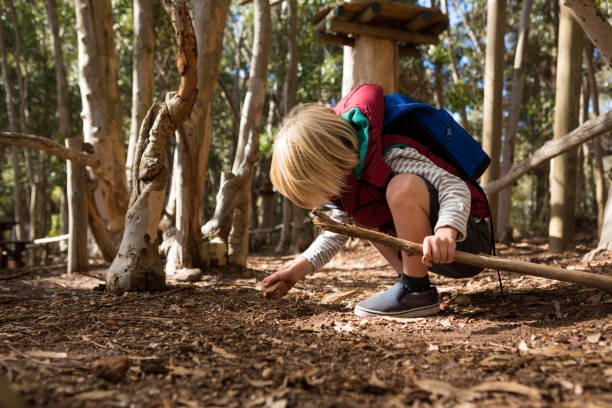 istock Little girl with backpack holding stick in her hand playing with rock 892955684