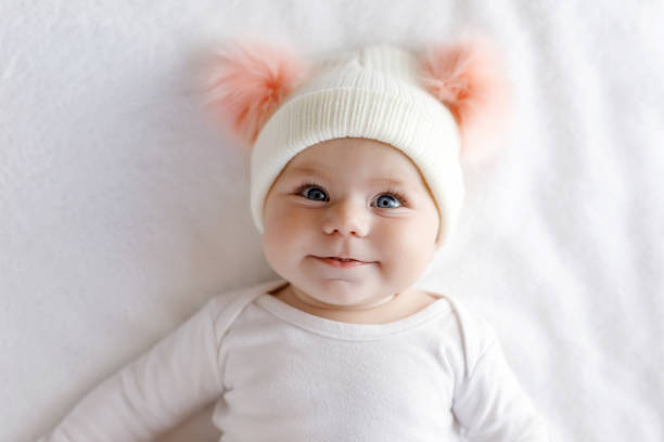 Cute adorable baby child with warm white and pink hat with cute bobbles Cute adorable baby child with warm white and pink hat with cute bobbles. Happy baby girl on white background and looking at the camera. Close-up for xmas holiday and family concept. baby girls stock pictures, royalty-free photos & images