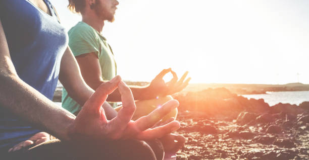 Couple doing yoga outdoor at sunrise in nature - Woman and man meditating together at morning time - Concept of fitness exercise for healthy lifestyle and positive mind - Focus on woman right hand Couple doing yoga outdoor at sunrise in nature - Woman and man meditating together at morning time - Concept of fitness exercise for healthy lifestyle and positive mind - Focus on woman right hand acroyoga stock pictures, royalty-free photos & images