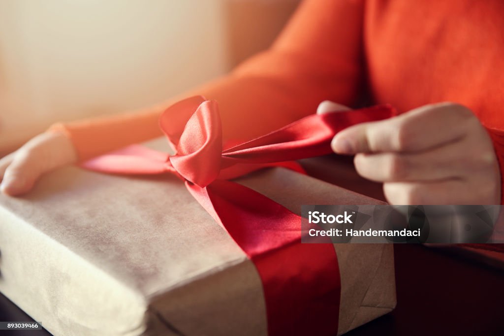 Hand pulls red ribbon on a gift wrapped in brown paper Box - Container, Holiday - Event, Event, Gift Box, Human Hand, Valentine's Day,  noel, New years Gift Stock Photo