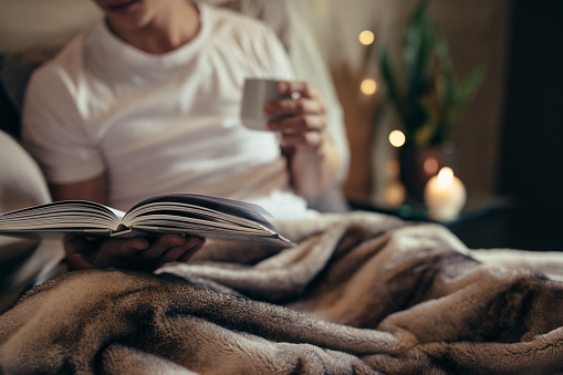 Close up of male on bed with open book and coffee. Man reading book on bed at home.