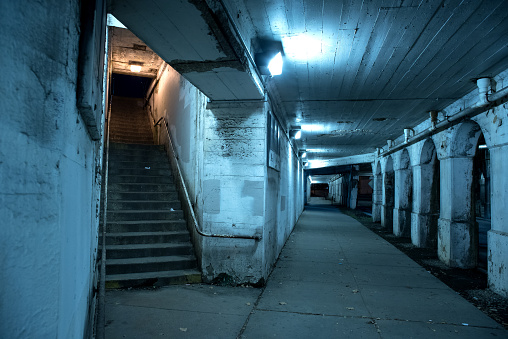 Gritty dark Chicago city street under industrial bridge viaduct tunnel with a stairway to Metra train station at night.