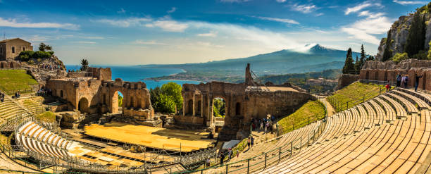 Panoramic view of the Ancient Theatre in Taormina, Sicily The Greek Theater in Taormina is a spectacular architectural sight. Its position is unique as it overlooks the beautiful Mediterranean sea and magnificent Mount Etna mt etna stock pictures, royalty-free photos & images