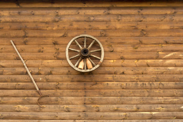 Traditional log house wall decorated with wooden wheel, pottery bottles and oven fork. Background with copy space. stock photo