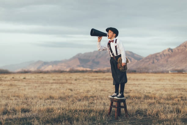 Old Fashioned News Boy Yelling Through Megaphone A news boy dressed in vintage knickers and newsboy hat stands yelling through a megaphone in the middle of a field in Utah, USA. He is trying to sell you what your business needs. gossip stock pictures, royalty-free photos & images