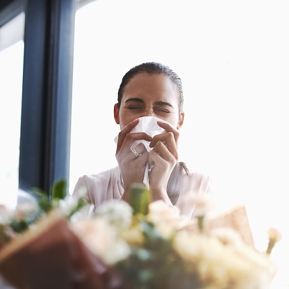 Shot of a young businesswoman blowing her nose in front of a bouquet of flowers
