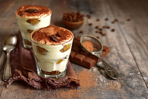 Homemade traditional italian dessert tiramisu with mascarpone cheese,savoyardi biscuit,coffee and whipped cream in a glasses over dark wooden background.