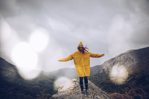 One woman, walking on mountain on a rainy day in yellow raincoat.