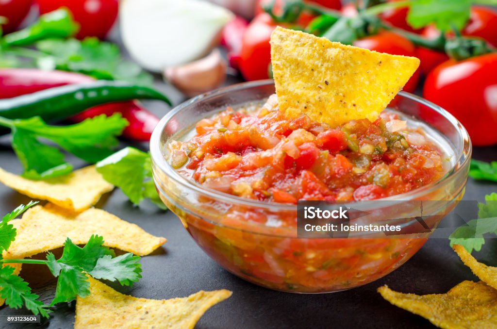 Traditional mexican homemade salsa sauce with ingredients, tomat Traditional mexican homemade salsa sauce with ingredients, tomatoes, pepper, cilantro, chips on a dark black stone table. Close-up, horizontal image Salsa Sauce Stock Photo