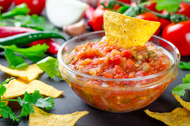 Traditional mexican homemade salsa sauce with ingredients, tomat Traditional mexican homemade salsa sauce with ingredients, tomatoes, pepper, cilantro, chips on a dark black stone table. Close-up, horizontal image tortilla chip photos stock pictures, royalty-free photos & images
