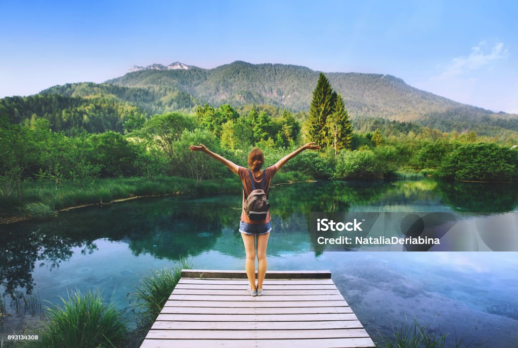 Mujer joven se levanta sobre un puente de madera con los brazos levantados en el fondo de la naturaleza. - Foto de stock de Mujeres libre de derechos