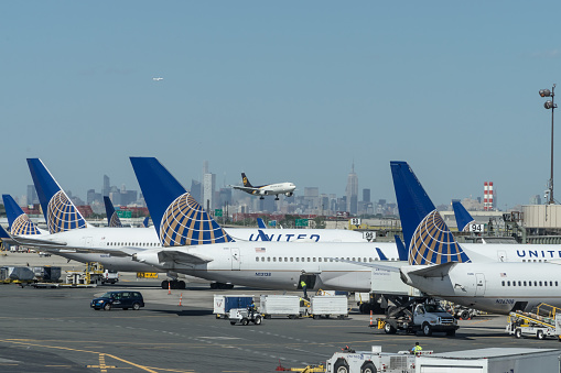 Newark, United States - September 6, 2016: Passenger jets belonging to United Airlines parked at gates 91 to 98 at Terminal C, Newark Liberty International Airport (EWR), New Jersey.  The jets are being serviced, loaded/unloaded and refuelled on the runway apron.  In the mid-distance a UPS freight jet is approaching the runway to land.  In the far distance is the skyline of Manhattan, New York.